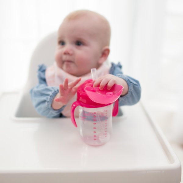 Baby sitting in highchair grabbing baby's first straw cup