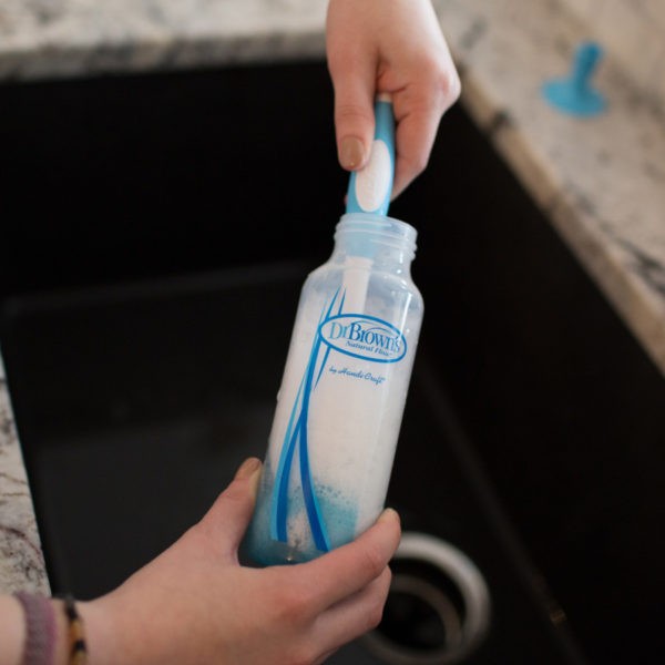 Up close image of woman washing bottle nipple with bottle brush