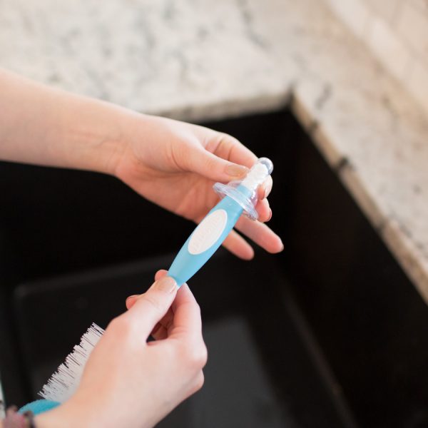 Up close image of woman washing bottle nipple with bottle brush