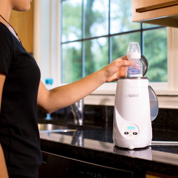 Woman putting bottle inside bottle warmer sitting on counter