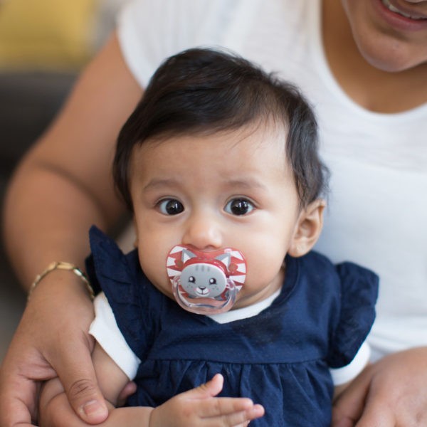 Baby in mother's lap with pink pacifier in mouth