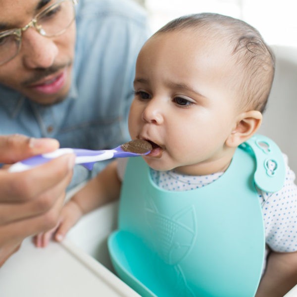 Baby in high chair being fed by dad with soft tip spoon