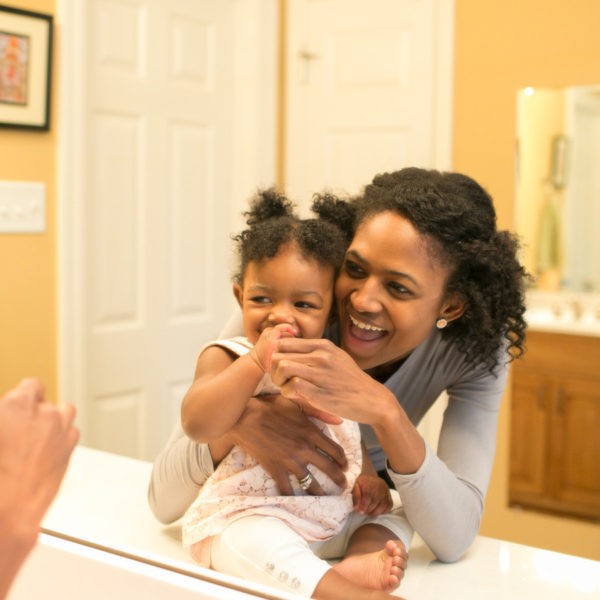 Baby and mother in bathroom brushing teeth with pink toothbrush