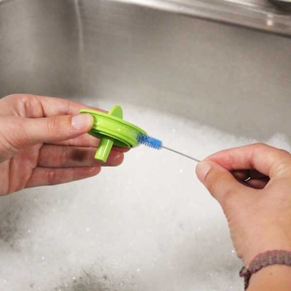 Woman washing bottles parts in sink with cleaning brush