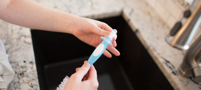 Woman washing bottle nipple with bottle brush in kitchen sink