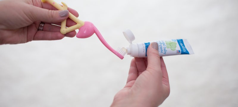 Hands putting toothpaste onto flamingo toothbrush