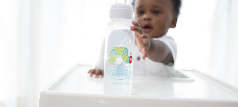 Baby sitting in high chair reaching for sippy bottle