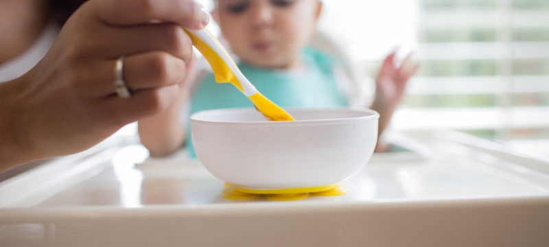 Mom feeding baby in highchair with soft tip spoon and suction bowl